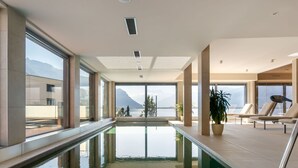 Een modern binnenzwembad met glazen wanden, uitzicht op bergen en ligbedden.