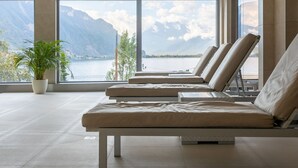 Een moderne kamer met grote ramen met uitzicht op een meer en bergen. Er staan drie comfortabele fauteuils.