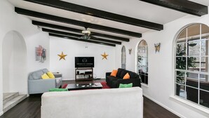 Una sala de estar moderna con techo negro, paredes blancas y un amplio ventanal arqueado. Se observan dos sofás, una mesa de centro y un televisor sobre un mueble.