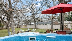 Un patio trasero con jacuzzi, mobiliario exterior y una sombrilla roja.