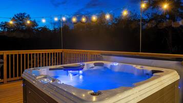 A hot tub on a wooden deck with string lights above.