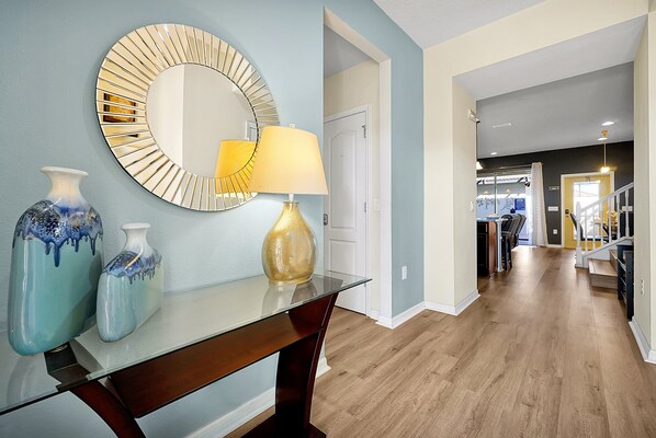 A hallway with a round mirror, two vases, and a lamp on a glass table. - Welcome to Paradise | Windsor at Westside Resort (Kissimmee)
