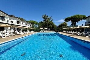A swimming pool with lounge chairs and umbrellas, surrounded by buildings and trees.