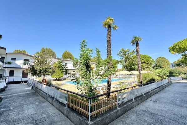 A rooftop pool area with palm trees, a white fence, and a clear blue sky.