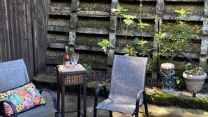 En terrasse med to stole, et lille bord med flaske og glas, samt en dekorativ stenvæg.