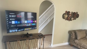 Sala de estar com televisão de tela plana presa a um console de madeira, sofá estampado e um objeto decorativo na parede.