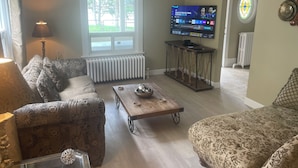 Sala de estar com sofá, mesa de centro, televisão em móvel, luminária e janela com vista para área verde.