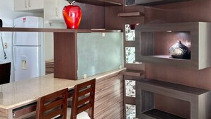 A modern kitchen with built-in wooden shelves, a granite countertop, and a red vase. - Deluxe Apartment with Guayas River view in Puerto Santa, Guayaquil (Guayaquil)