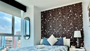 A modern bedroom with a large bed, a nightstand, a lamp, and a view of the city through a large window. - Deluxe Apartment with Guayas River view in Puerto Santa, Guayaquil (Guayaquil)