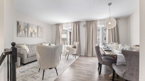 A spacious living room with a sofa, chairs, a dining table set for six, and a large window with curtains.