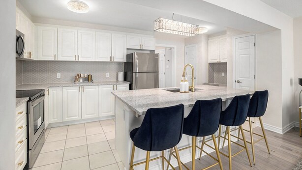 A modern kitchen with white cabinets, a central island with bar stools, stainless steel appliances, and a chandelier.