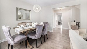 A dining area with a wooden table, four upholstered chairs, a chandelier, and a mirror on the wall.