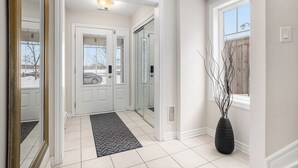 A clean, modern hallway with white walls, a tiled floor, and a black rug leading to a door.