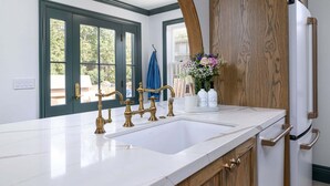 A kitchen with a white marble countertop, brass faucets, wooden cabinets, and a built-in refrigerator. - Beautiful Magical Historic Webster House at Eleison Farms - Avocado Ranch 3 BD/2 BA (Carpinteria)