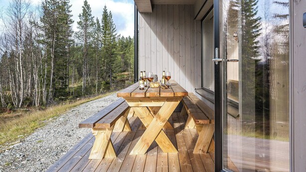 Een houten terras met een picknicktafel en banken, omgeven door een bos.