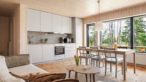 Een moderne keuken met witte kasten, een eethoek met een tafel en stoelen, en een groot raam met uitzicht op bomen.