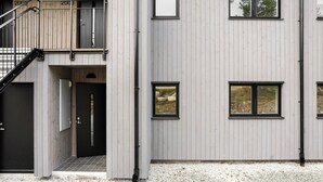 Een modern gebouw met een grijze gevel, meerdere ramen en een trap die naar een hoger niveau leidt.