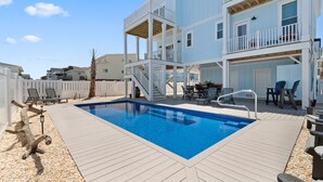 A pool area with a wooden deck, a white fence, and a two-story building with balconies. - "Holden Memories" is a 5 Bedroom Second Row Home w/ PRIVATE Pool! (Holden Beach)