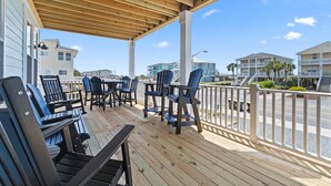 A covered outdoor seating area with wooden tables and chairs, overlooking a street with buildings and a clear sky. - "Holden Memories" is a 5 Bedroom Second Row Home w/ PRIVATE Pool! (Holden Beach)