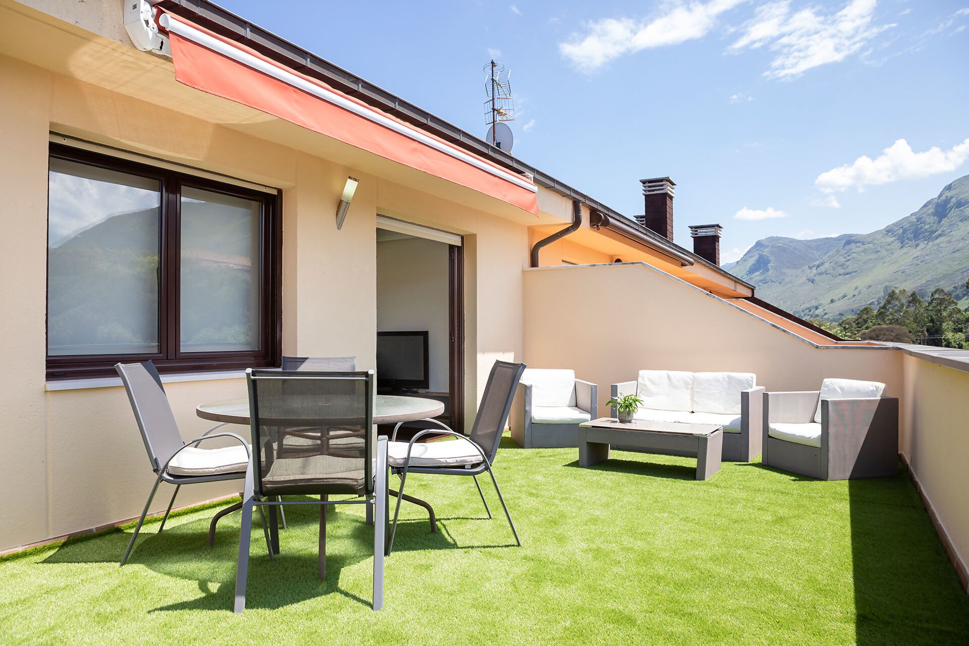 A balcony with a table and chairs, a small table with a plant, and a view of mountains.
