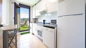 Una cocina moderna con electrodomésticos blancos, un comedor con mesa y sillas, y vistas a un jardín verde a través de una puerta de vidrio.