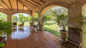 Eine überdachte Terrasse mit Steinbögen, Gartenmöbeln und Topfpflanzen.