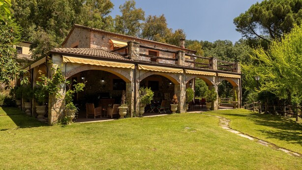Ein Steinhaus mit einer überdachten Terrasse, Sitzgelegenheiten im Freien und einem Garten.