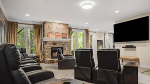 A home theater room with a stone fireplace, leather recliners, a flat-screen TV, and a large window. - Hot Tub-Movie Rm-Game Rm (Asheville)