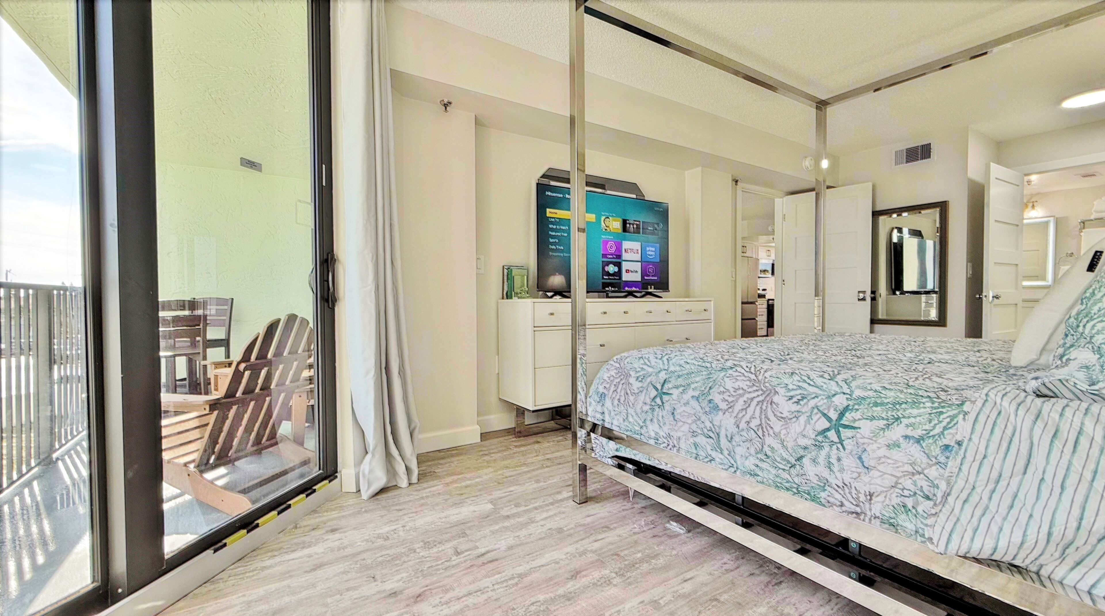 A bedroom with a bed, a TV, a desk, and a balcony.