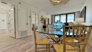 A dining area with a glass table surrounded by bamboo chairs, a blue vase, and a modern chandelier.
