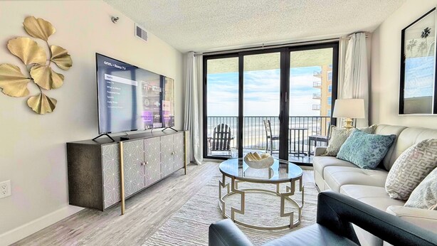 A modern living room with a flat-screen TV, a glass coffee table, and a sofa.