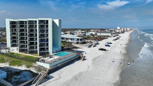 A multi-story hotel with balconies, a pool, and a beach view.