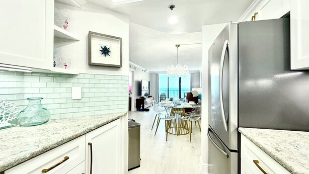 Una cocina moderna con armarios blancos, un refrigerador de acero inoxidable y una zona de comedor con candelabro.