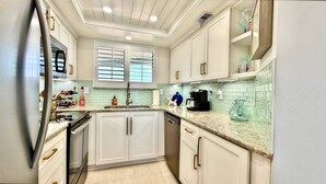 Una cocina con armarios blancos, un refrigerador de acero inoxidable, lavavajillas y una ventana con persianas.