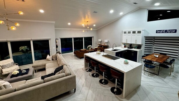 A modern kitchen with a central island, a dining area with a wooden table, and a living room with a beige sofa.
