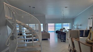 A modern interior with a spiral staircase, a dining area with bar stools, and a view of the ocean.