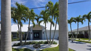 A modern building with a white facade, palm trees, and a well-maintained lawn.