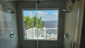 A modern bathroom with a large window, a shower area, and a view of a balcony and greenery.