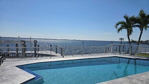 A rectangular pool with a clear blue water surface, surrounded by a white metal railing and a stone deck.