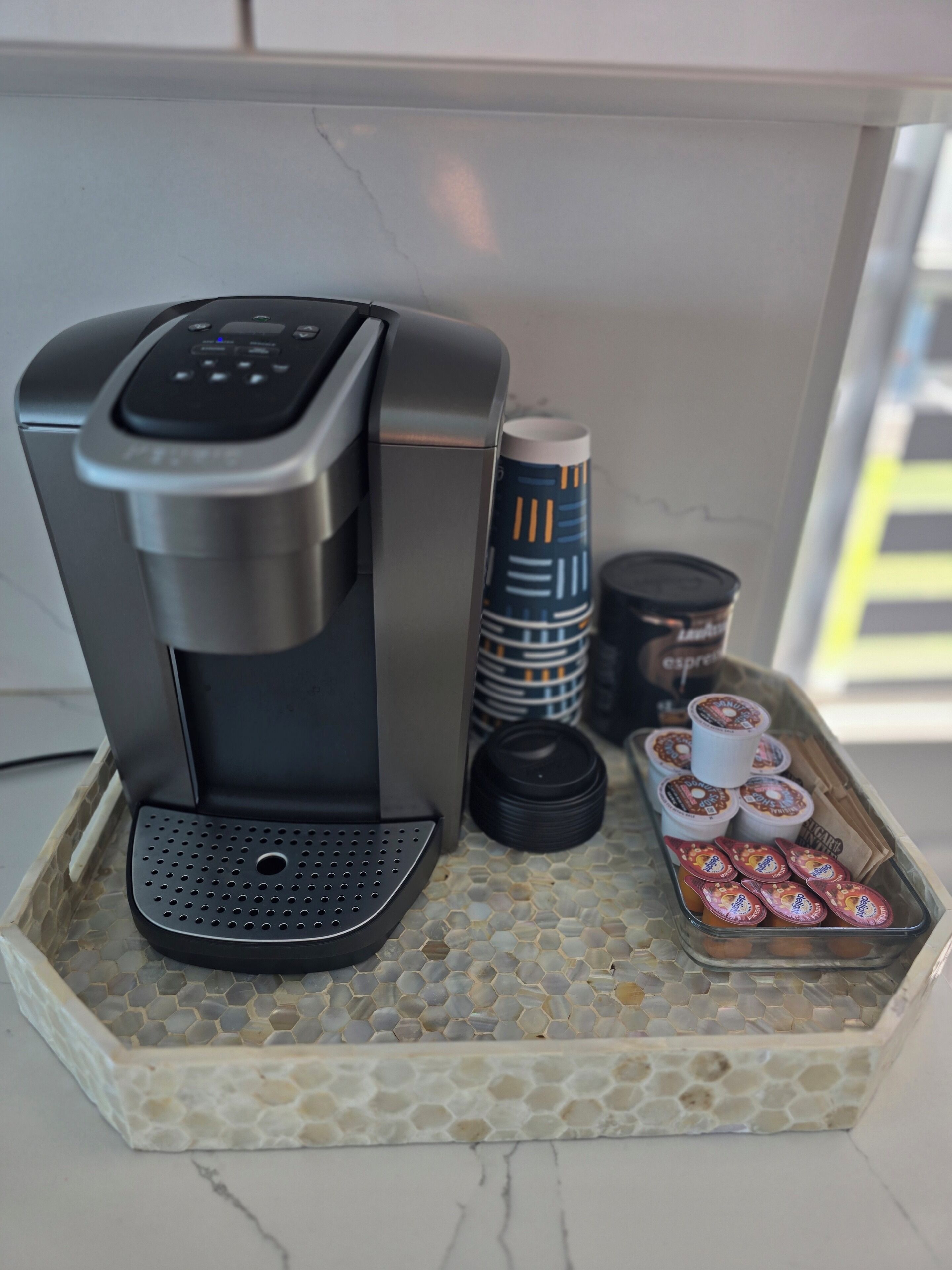 A coffee machine on a tray with disposable cups and a stack of tumblers.