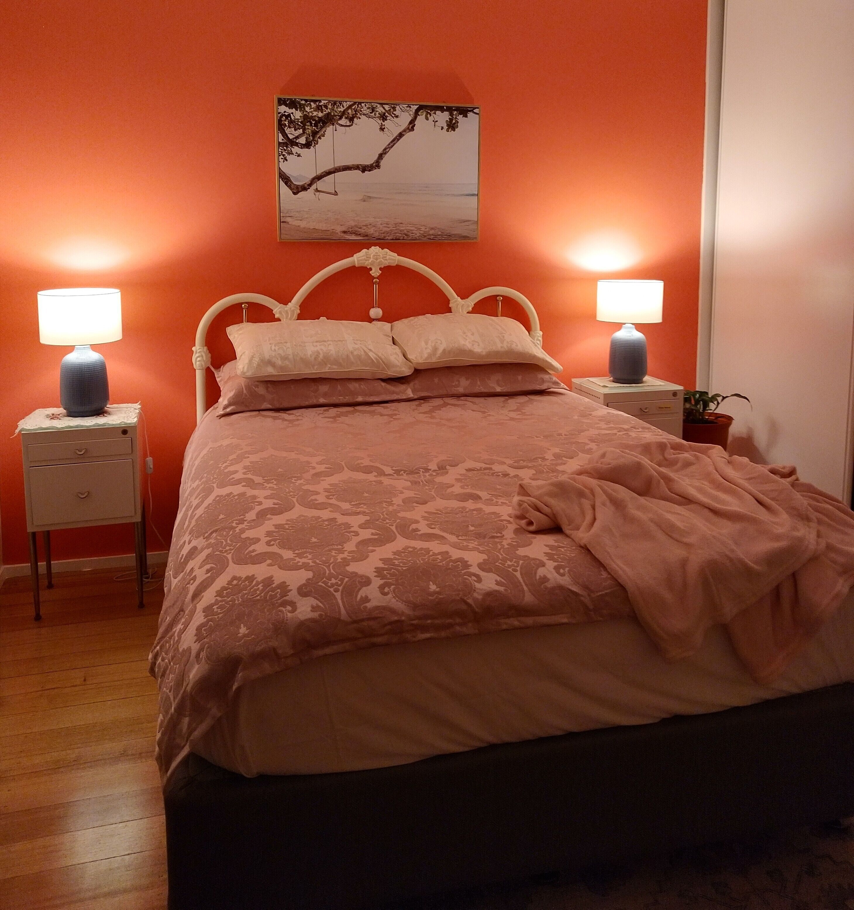 Ein Schlafzimmer mit einem Bett, zwei Nachttischen, einem Wandbild und einem Blumentopf.