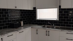A modern kitchen with white cabinets, black tiled backsplash, and a window with blinds. - Cosy Corio Gateway - 2 Mins to Spirit of Tasmania (Corio)