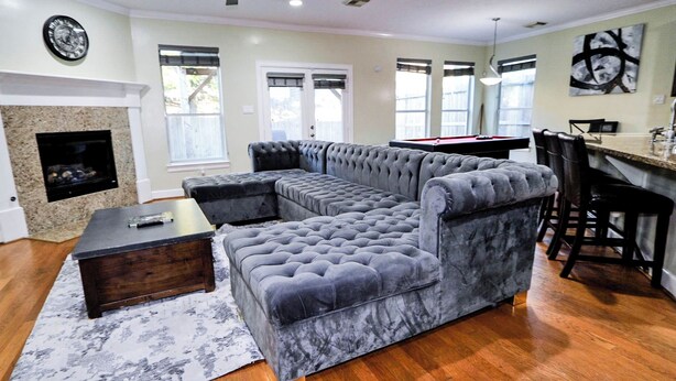 A living room with a sectional sofa, a fireplace, and a dining area with bar stools. - Spacious Family Gem: Near NRG Stadium-Med Center - Pool Table - BBQ -11guests (Houston)