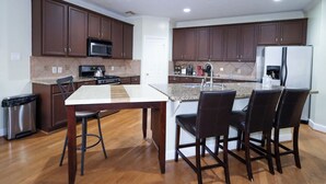 A modern kitchen with dark wooden cabinets, a stainless steel refrigerator, a microwave, and a granite countertop. - Spacious Family Gem: Near NRG Stadium-Med Center - Pool Table - BBQ -11guests (Houston)