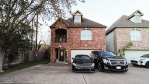 A two-story brick house with a garage, a driveway, and three luxury vehicles parked in front. - Spacious Family Gem: Near NRG Stadium-Med Center - Pool Table - BBQ -11guests (Houston)
