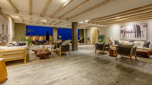 A spacious living area with a high ceiling, wooden beams, and a view of the beach at dusk. - Beachfront, Ocean View, Amazing Location! (San José del Cabo)