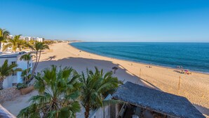 A beach with a clear sky, palm trees, and a building with a thatched roof. - Beachfront, Ocean View, Amazing Location! (San José del Cabo)