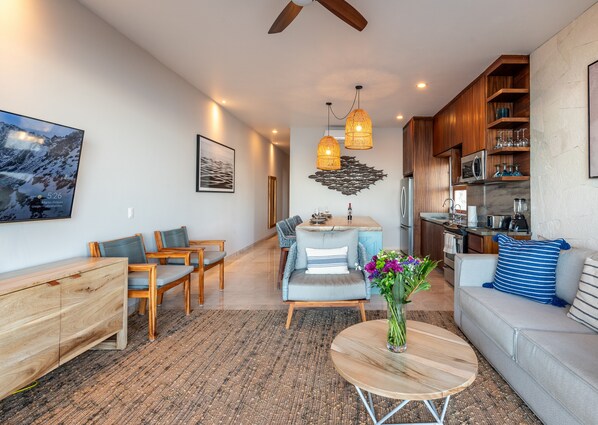 A modern living room with a sofa, chairs, a coffee table, and a kitchen area with wooden cabinets and appliances. - Beachfront, Ocean View, Amazing Location! (San José del Cabo)