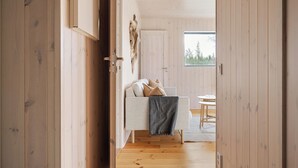 A wooden interior with a sofa and a table, a window with a view of trees, and a door leading to another room. - Renstråket 1001 by Interhome (Tännäskröket)
