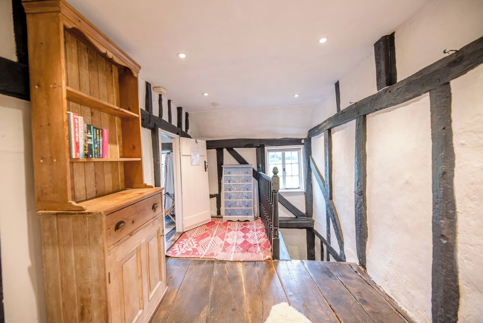A narrow hallway with wooden paneling, a staircase, and a red patterned rug.